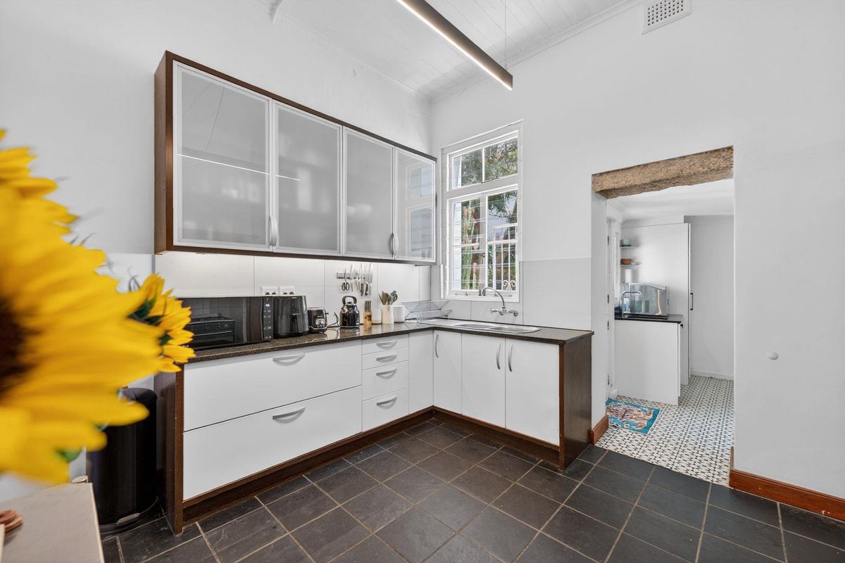 A well-maintained kitchen featuring modern white cabinetry with frosted glass uppers, dark stone countertops, and a distinct timber ceiling with linear lighting.