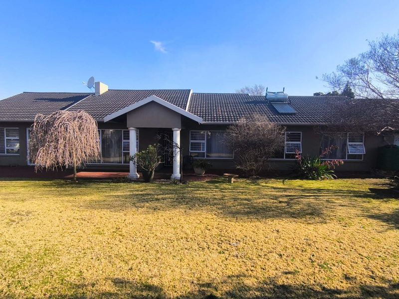 A single-story residential home featuring a tiled roof, solar water heating system, covered entrance porch with columns, and a spacious front lawn.