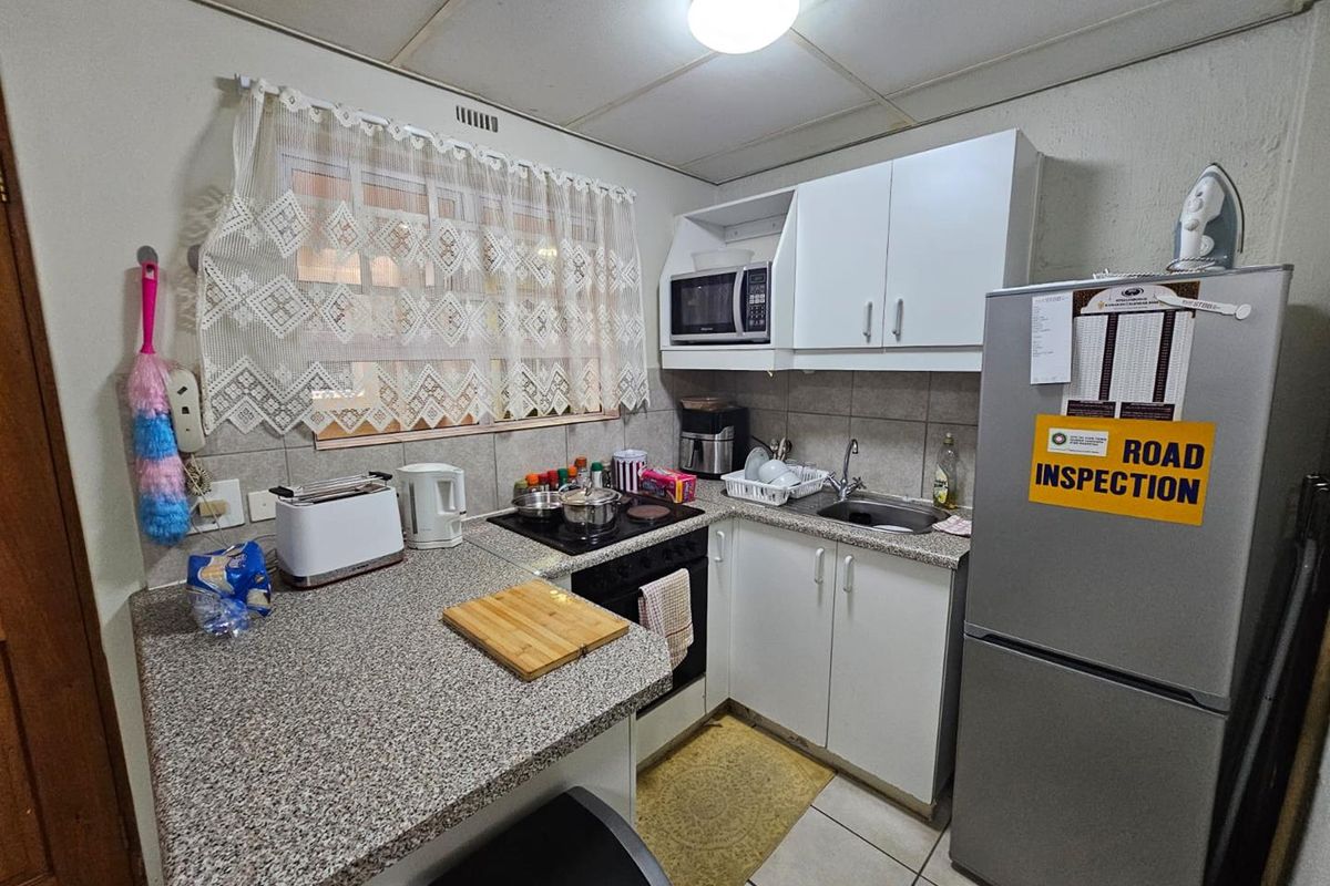 Compact kitchen featuring white cabinetry, granite-look laminate countertops, built-in oven and hob, and tiled flooring in a functional apartment layout.