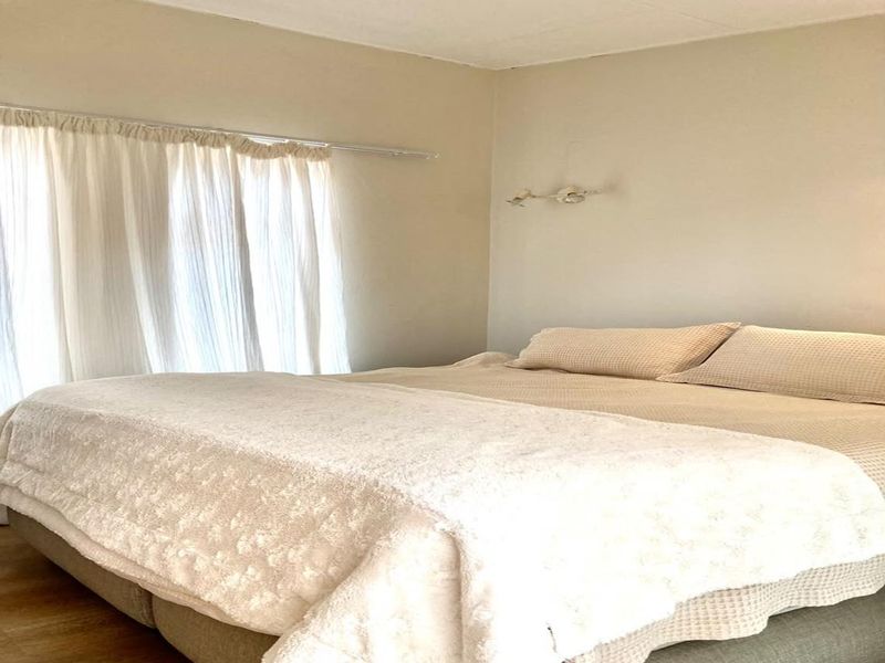 A neutrally decorated bedroom featuring a wall-mounted light fixture and window treatments, offering a clean and simple space.