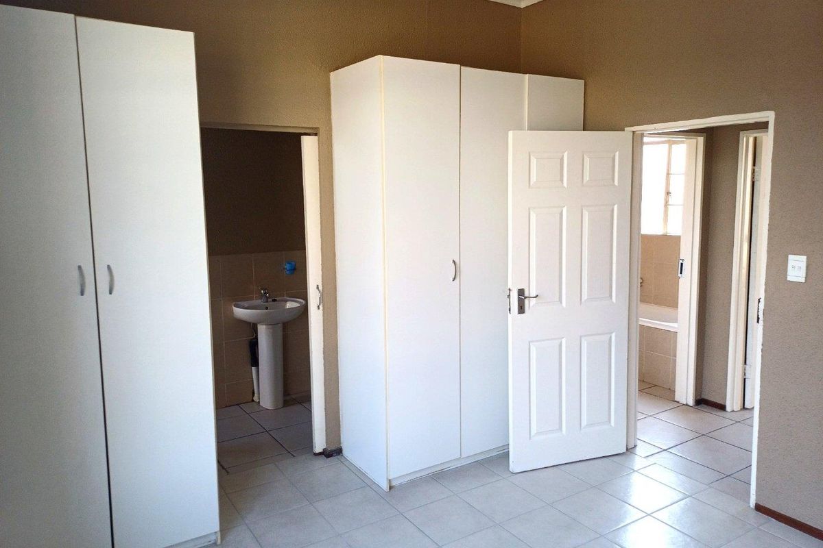 Spacious bedroom featuring built-in cupboards, tiled flooring, and direct access to an en-suite bathroom with a pedestal basin and bathtub.