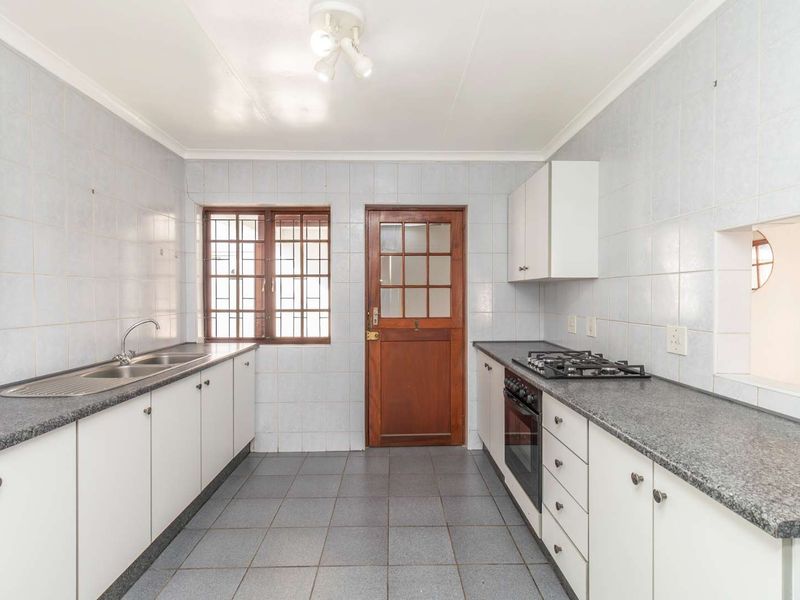 A functional kitchen featuring built-in cabinetry, a gas hob, an oven, and tiled finishes throughout, offering a clean and practical workspace.