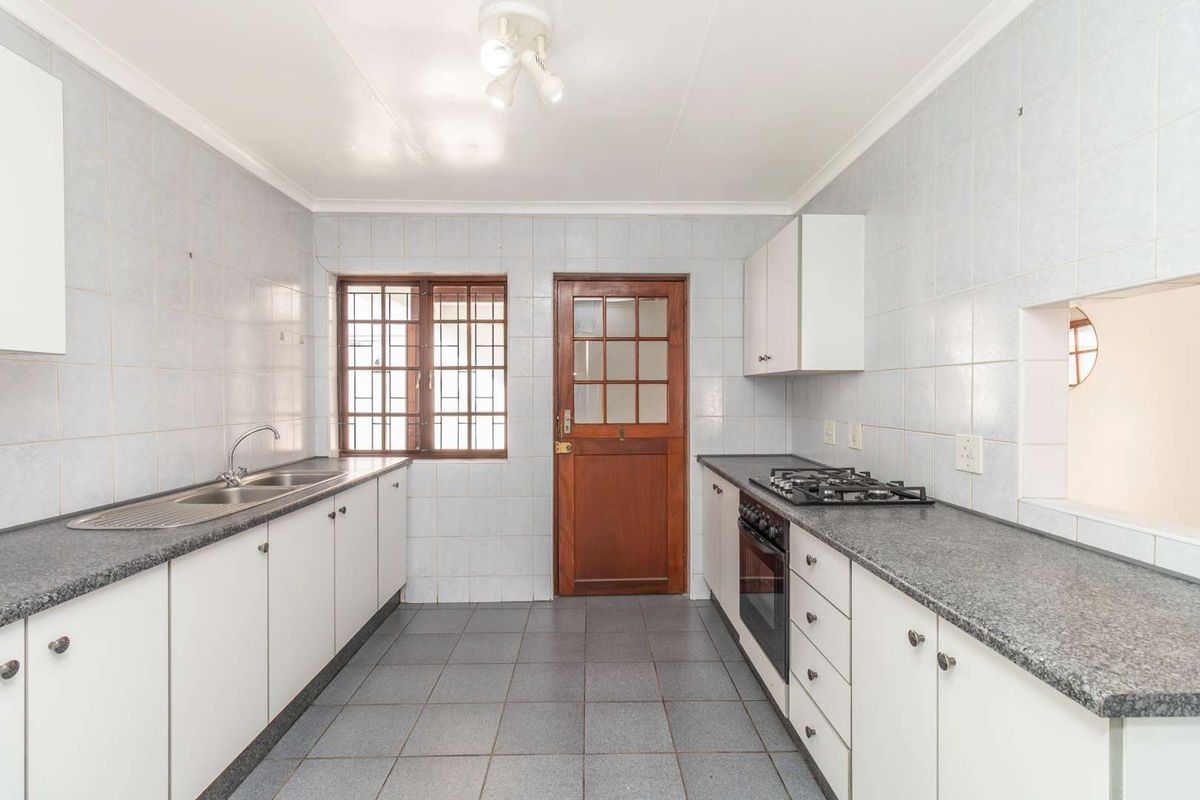 A functional kitchen featuring built-in cabinetry, a gas hob, an oven, and tiled finishes throughout, offering a clean and practical workspace.