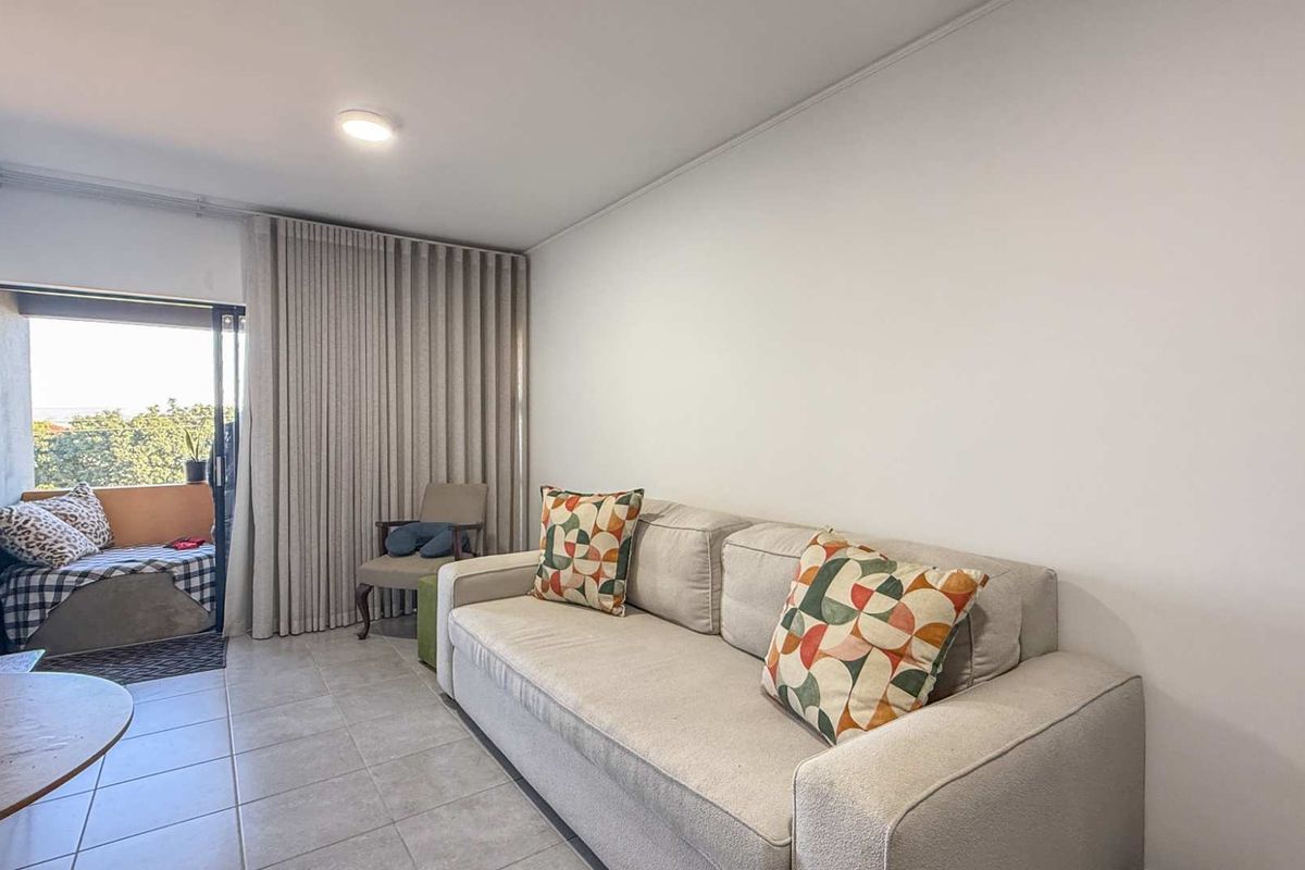 A bright living room featuring tiled flooring and large sliding glass doors that open onto a private balcony.