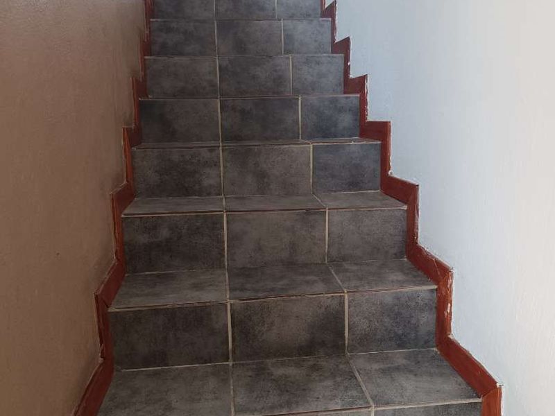 A staircase featuring dark grey floor tiles and painted skirting boards leading to an upper level.