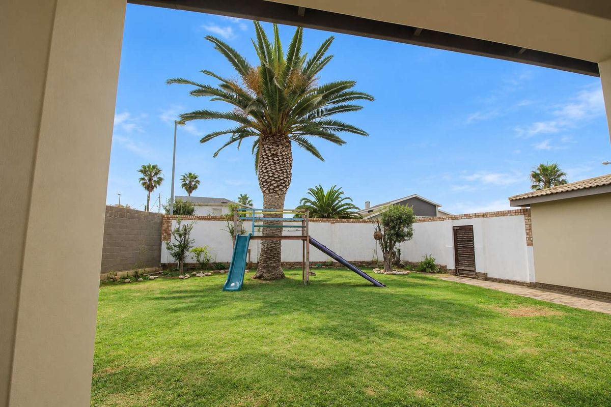 A private rear garden featuring a well-maintained lawn, perimeter boundary walls, and a paved walkway, viewed from a covered patio area.