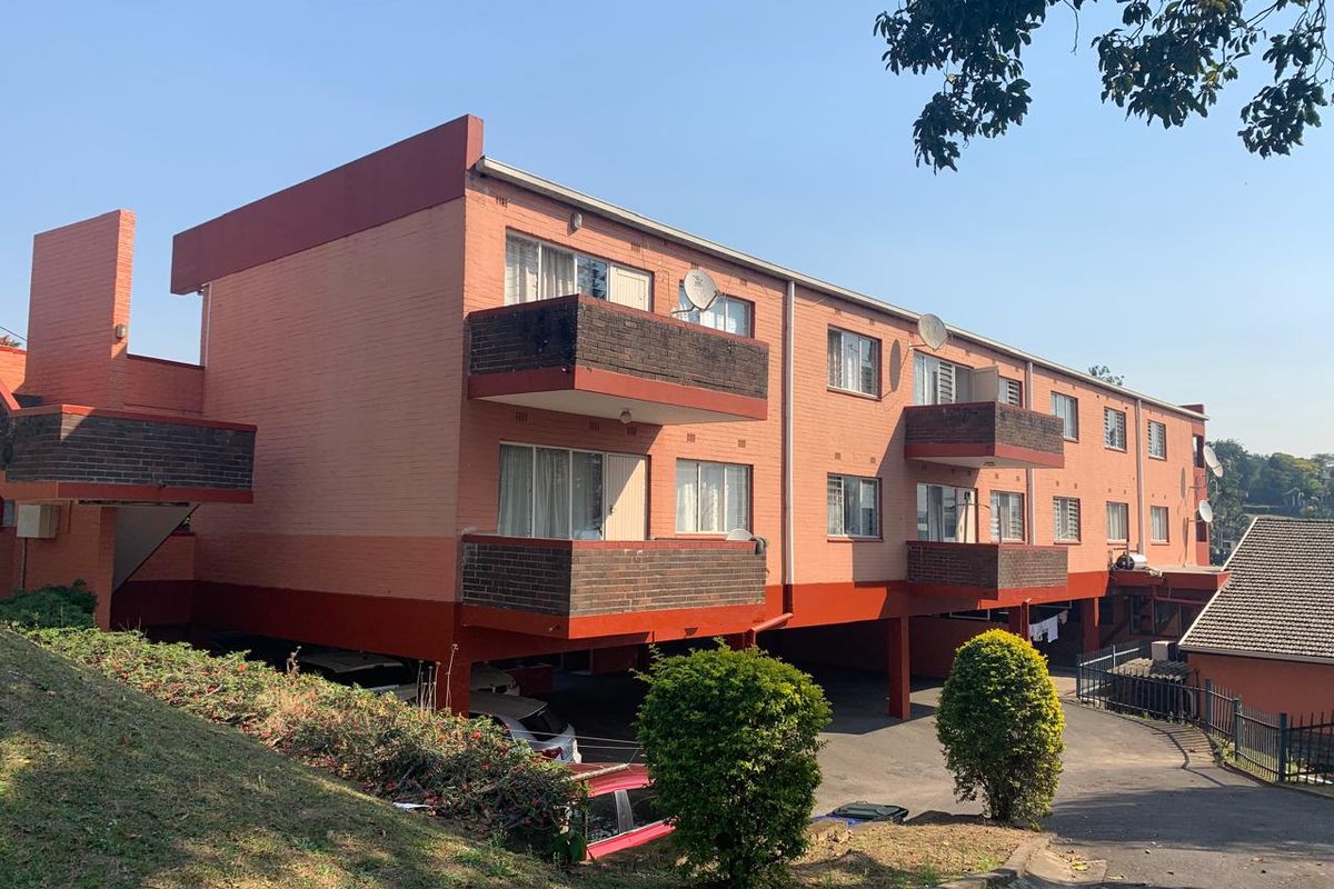 Rear view of a multi-story apartment complex featuring brick facade, private balconies, and a covered ground-level parking area.