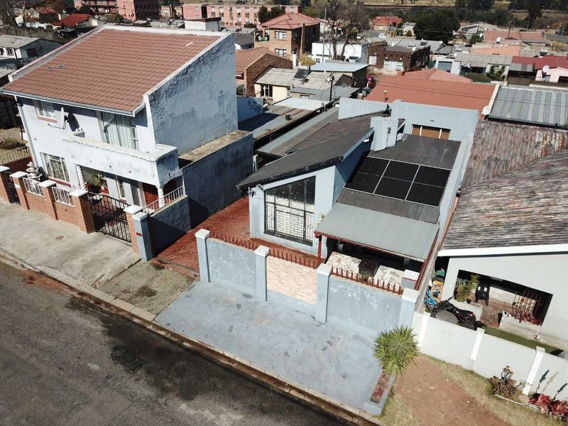 Aerial view of a residential property featuring a tiled roof, installed solar panels, a paved driveway, and a secure perimeter wall with gated access.