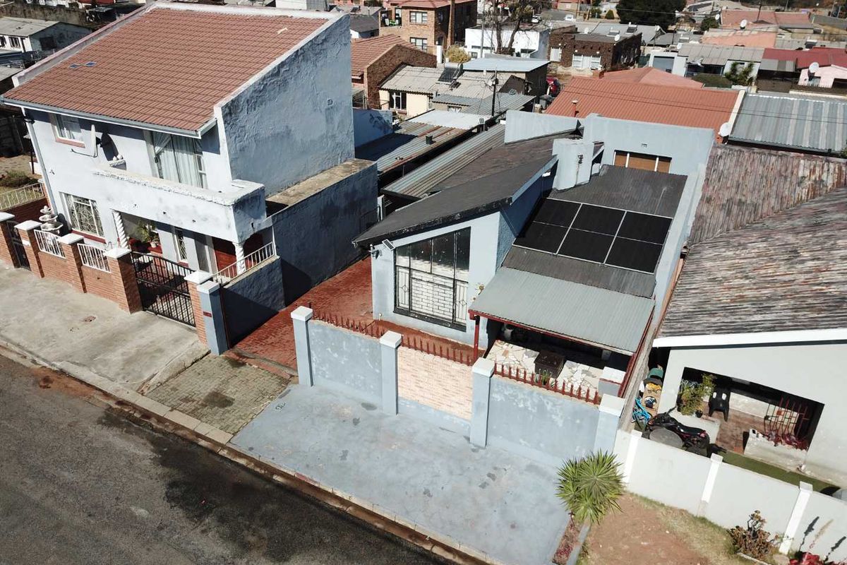 Aerial view of a residential property featuring a tiled roof, installed solar panels, a paved driveway, and a secure perimeter wall with gated access.