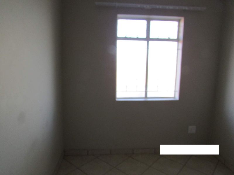 A simple, empty bedroom featuring tiled flooring and a window with security bars, providing a neutral space ready for personalization.