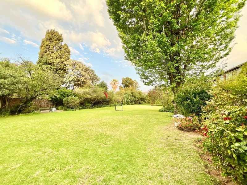 A spacious, well-maintained private garden featuring a large lawn area surrounded by mature trees and established landscaping.