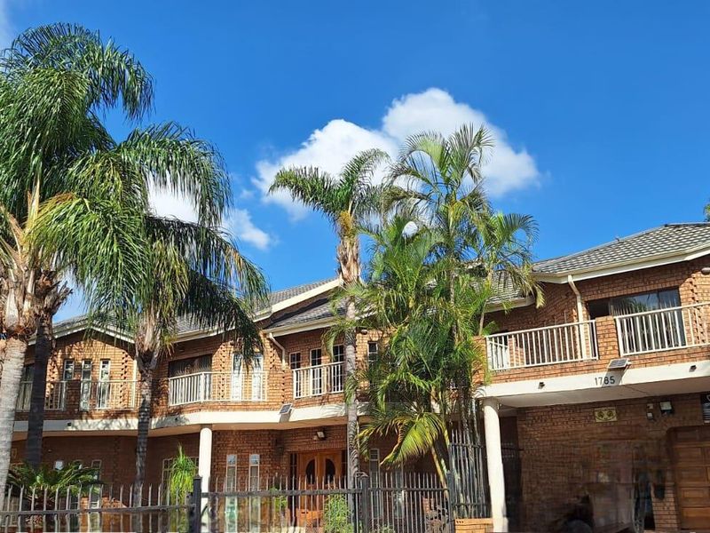 A multi-story face brick residential property featuring a tiled roof, upper-level balconies with metal railings, and a secure gated entrance.