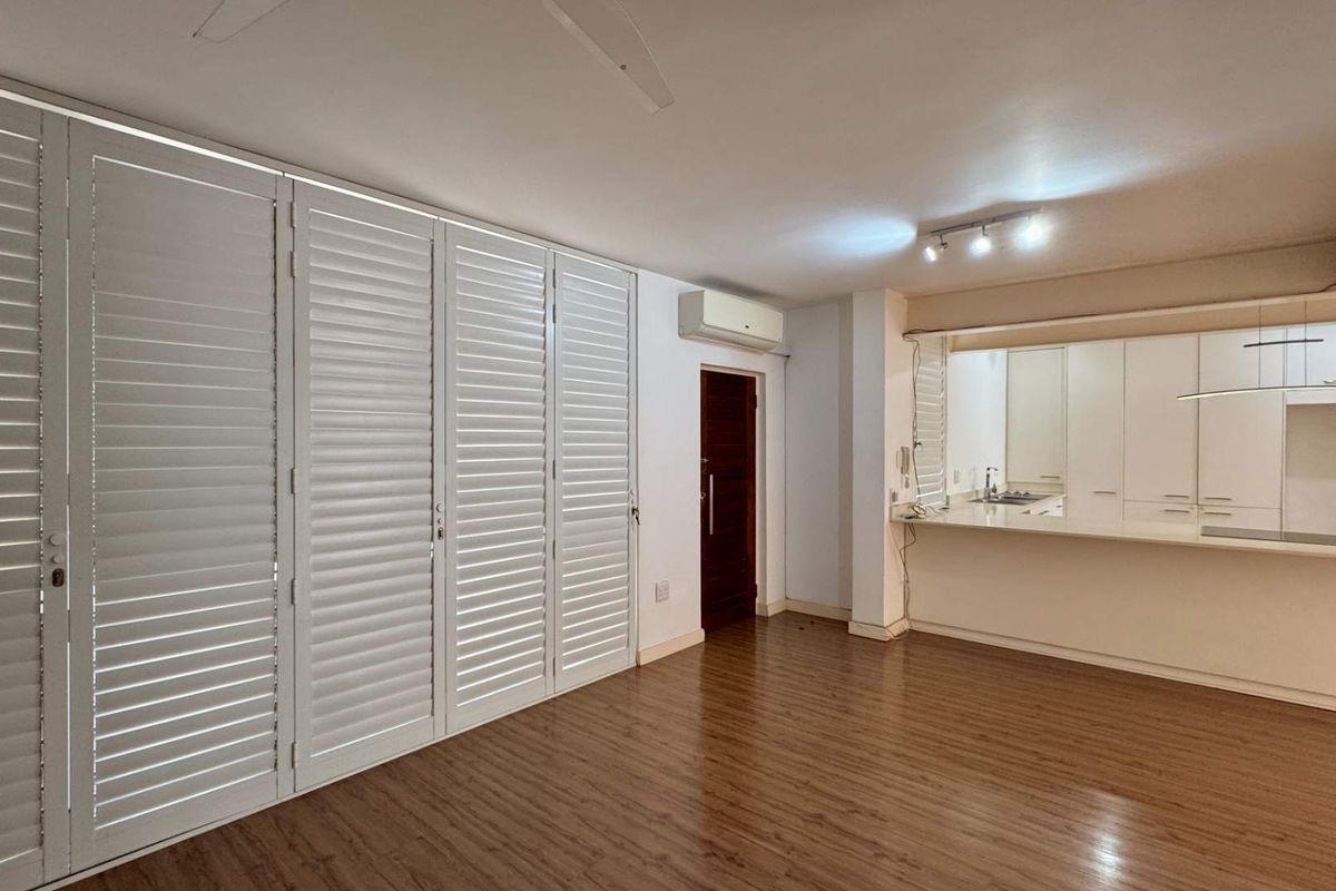 Spacious open-plan living area featuring laminate flooring, white plantation shutters, a split-system air conditioner, and an integrated kitchen with a breakfast bar.