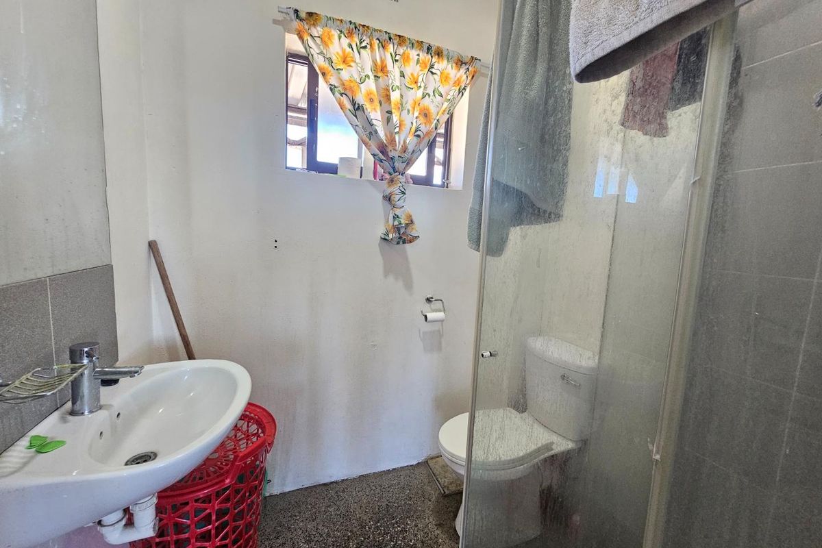 A functional bathroom featuring a pedestal basin, a toilet, and a glass-enclosed shower area with a small ventilation window.