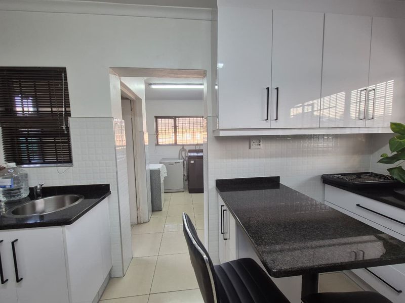 Modern kitchen featuring gloss white cabinetry, dark granite countertops, tiled backsplash, and a convenient pass-through to the adjacent laundry area.