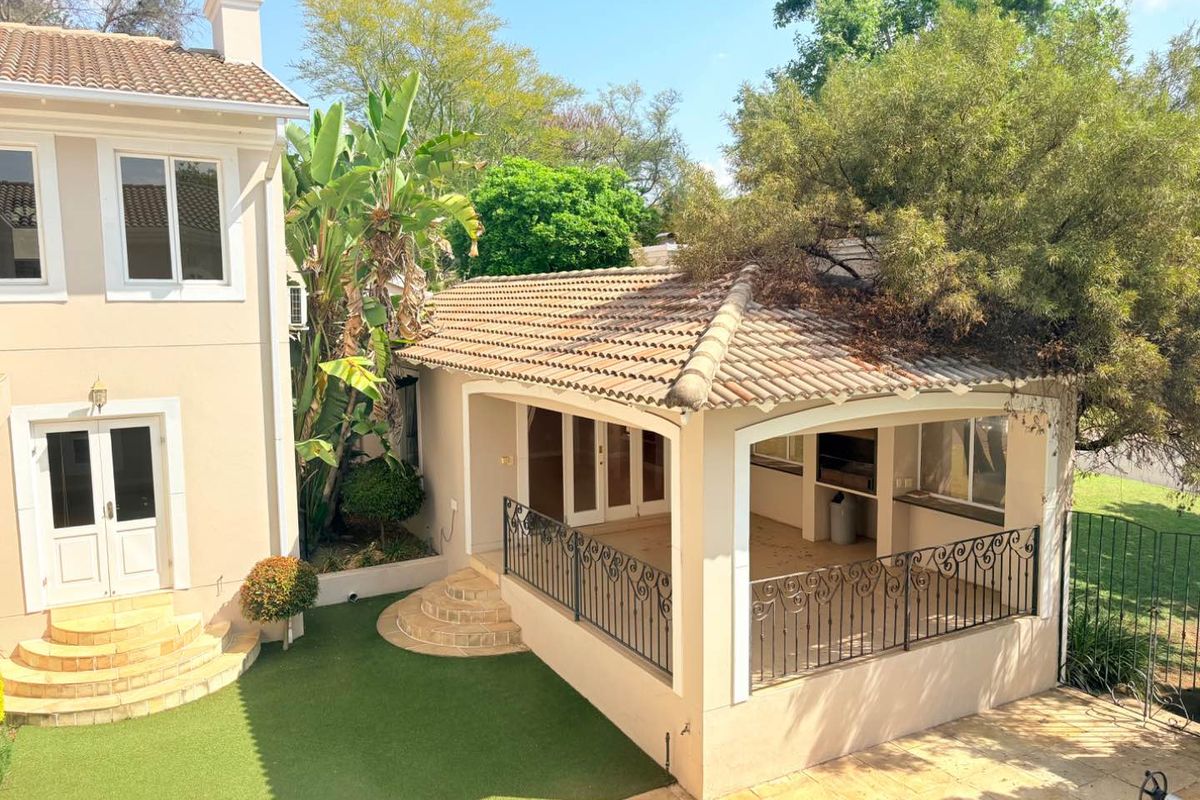 Rear view of the property featuring a covered patio with a built-in braai, wrought iron railings, and a well-maintained garden area.