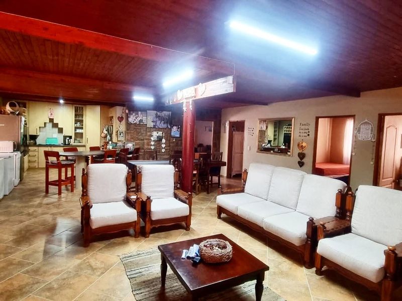 Spacious open-plan living area featuring exposed timber ceiling beams, tiled flooring, and a stone feature wall, seamlessly connecting to the kitchen space.