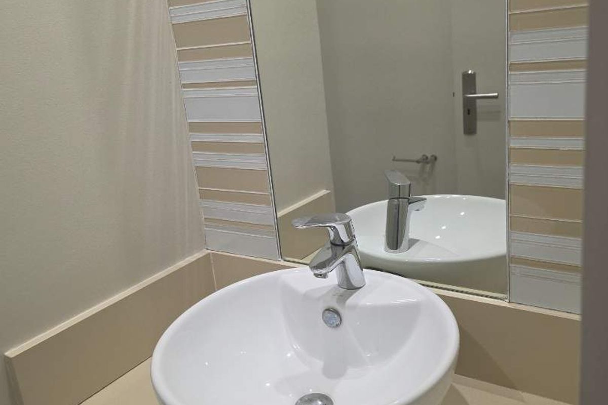 A clean and modern bathroom vanity featuring a white vessel sink, chrome mixer tap, and decorative tiled splashback with a wall-mounted mirror.