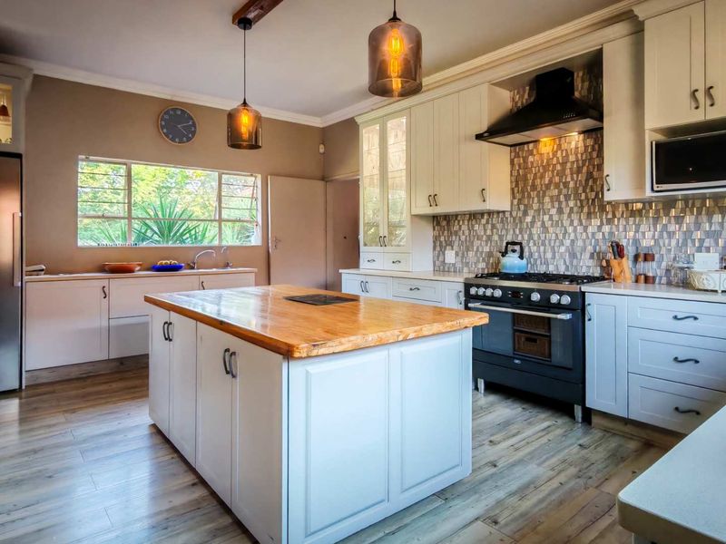 A well-appointed kitchen featuring a central island with a wooden countertop, modern cabinetry, a gas stove with an extractor fan, and stylish pendant lighting.