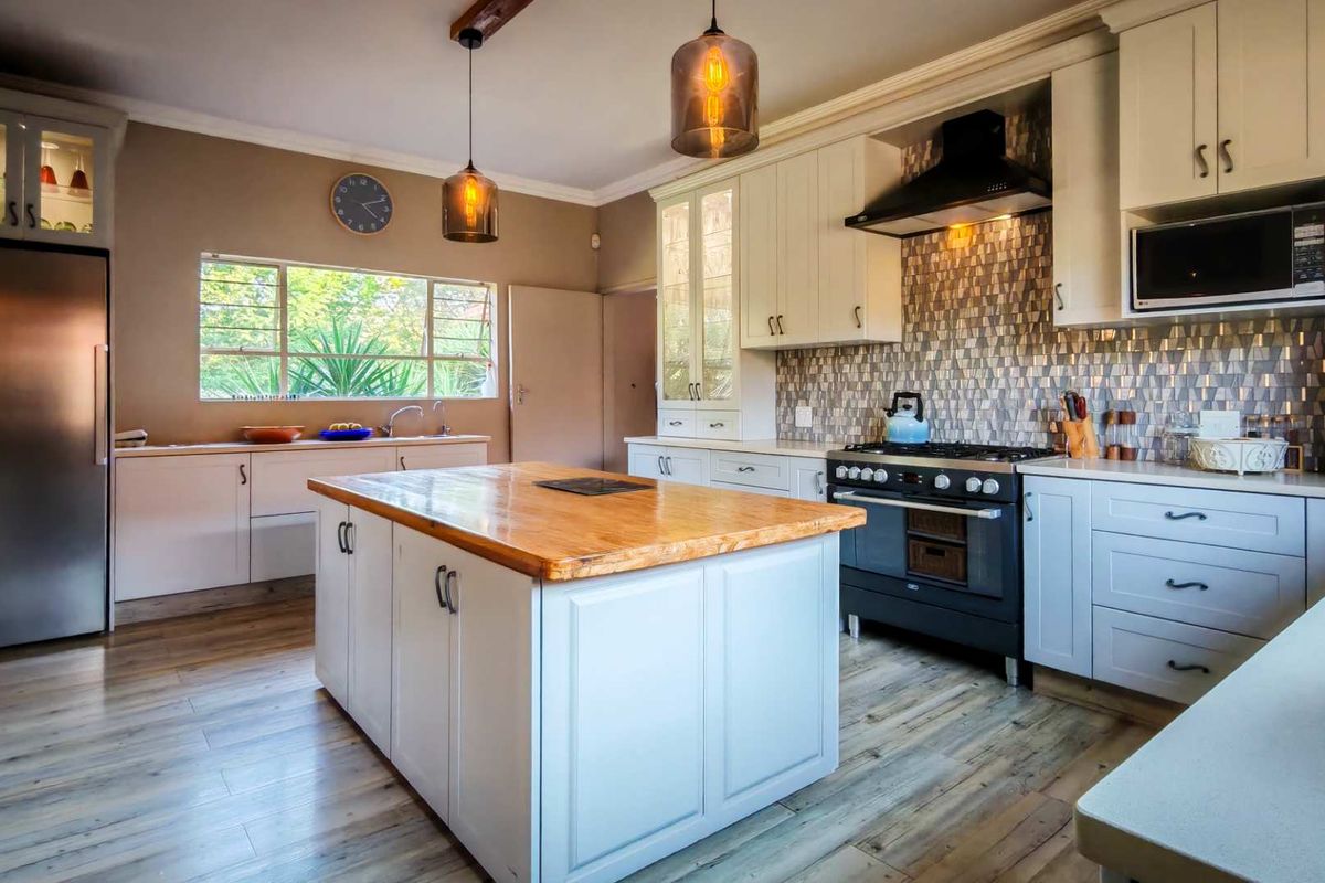 A well-appointed kitchen featuring a central island with a wooden countertop, modern cabinetry, a gas stove with an extractor fan, and stylish pendant lighting.