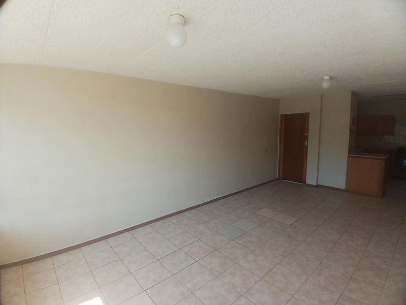 An empty open-plan living and kitchen area featuring tiled flooring, textured ceilings, and basic cabinetry, offering a blank canvas for renovation.