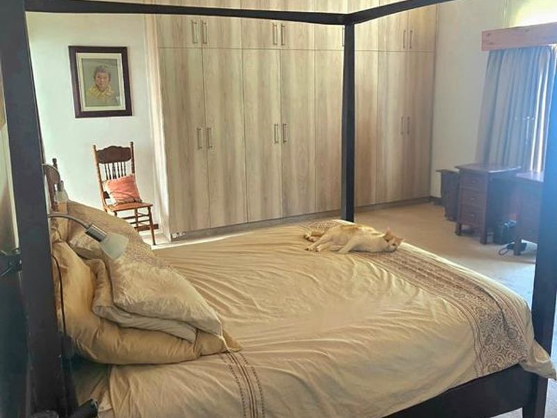 Spacious bedroom featuring exposed timber ceiling beams and extensive built-in wardrobe storage with neutral finishes.