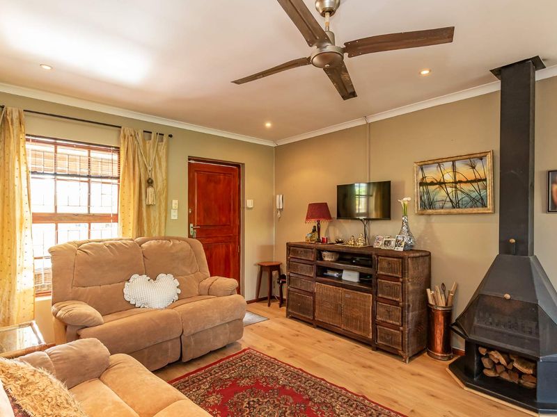 A cozy living room featuring laminate flooring, a ceiling fan, and a prominent freestanding fireplace, creating a warm and inviting atmosphere.