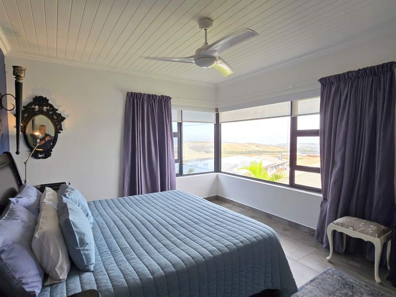 A well-lit bedroom featuring a tongue and groove ceiling, ceiling fan, and corner windows offering expansive views.