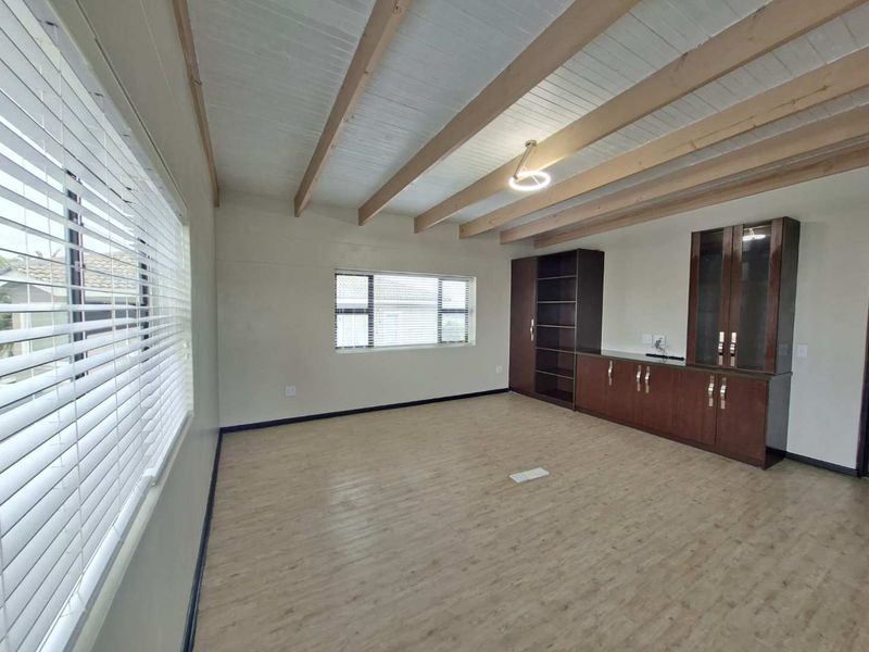 Spacious living area featuring exposed timber ceiling beams, light-toned laminate flooring, and extensive built-in cabinetry for storage.