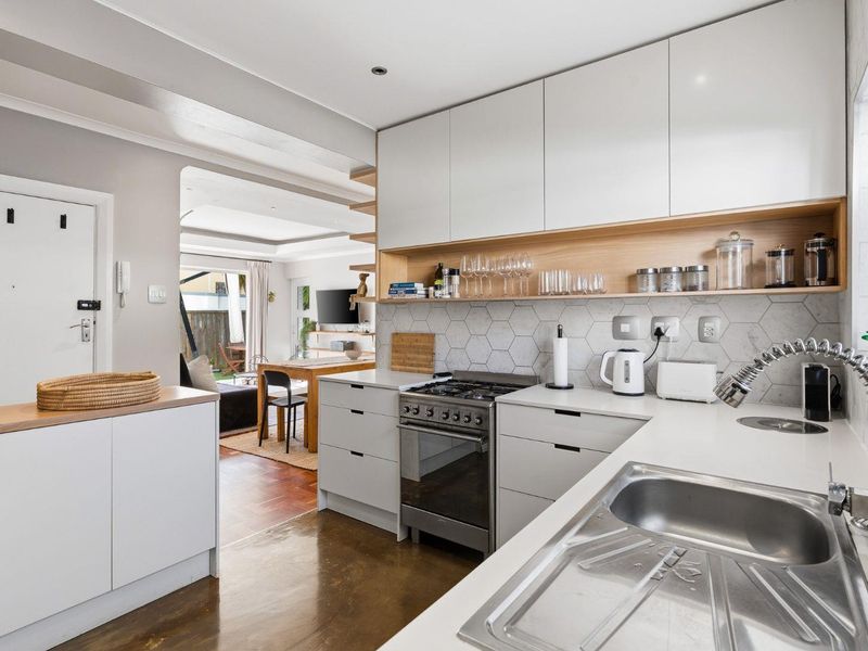 Modern kitchen featuring white cabinetry, stone countertops, a gas stove, and a stylish hexagonal tile backsplash, seamlessly flowing into the adjacent living area.