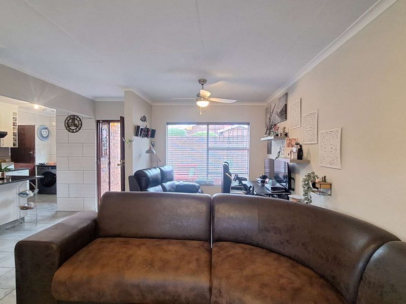 Open-plan living area featuring tiled flooring, a ceiling fan, and direct access to the kitchen and exterior entrance.