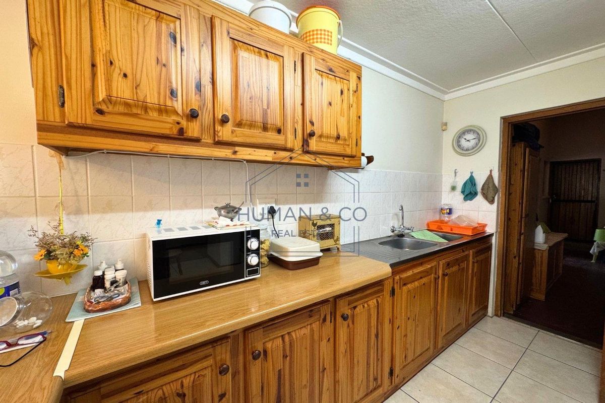 A functional kitchen featuring traditional timber cabinetry, tiled splashbacks, a stainless steel sink, and tiled flooring.