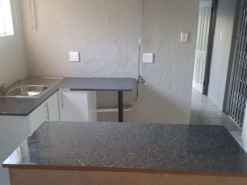 A compact kitchen area featuring granite countertops, a stainless steel sink, and built-in cabinetry, currently in need of finishing touches and cosmetic updates.
