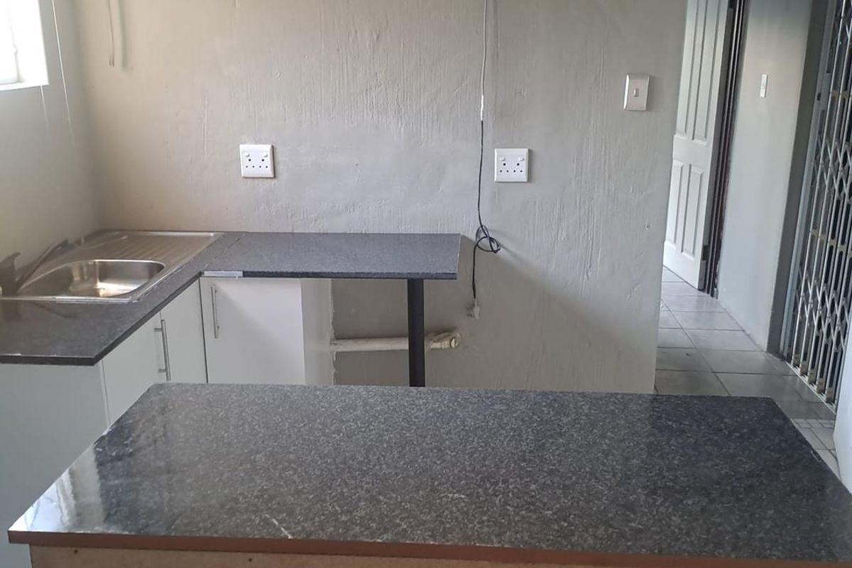 A compact kitchen area featuring granite countertops, a stainless steel sink, and built-in cabinetry, currently in need of finishing touches and cosmetic updates.