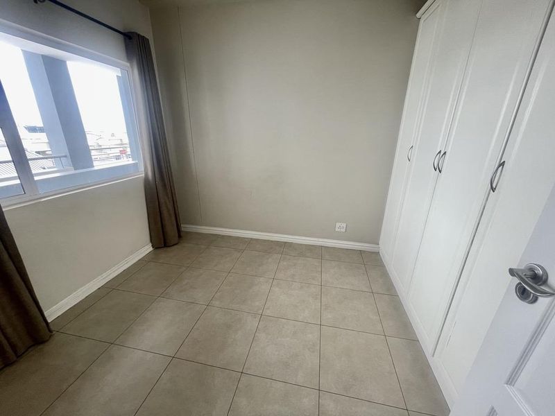 A clean, empty bedroom featuring neutral tiled flooring and white built-in cupboards, offering a versatile space ready for personalization.