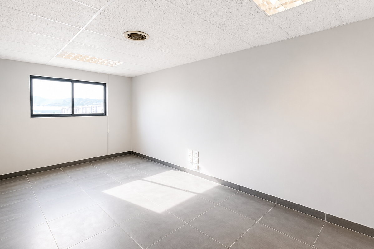 A clean, empty office space featuring neutral tiled flooring, a suspended ceiling with recessed lighting, and a sliding window providing natural light.