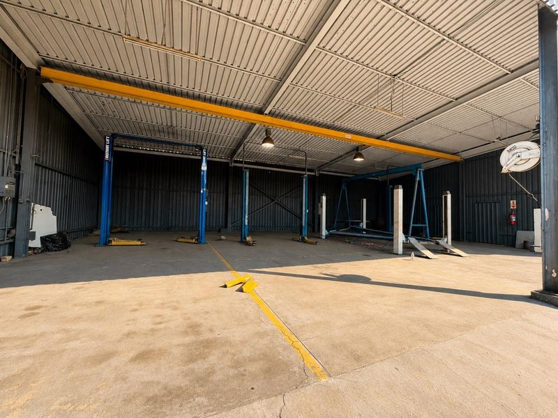 Spacious industrial garage facility featuring multiple vehicle lifts, an overhead crane, concrete flooring, and high-clearance corrugated metal roofing.
