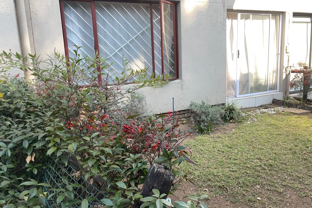 Rear exterior view of the apartment featuring a small garden, sliding glass door access, and windows with security bars.