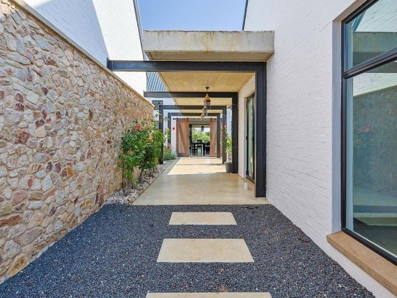 A modern covered walkway featuring stone cladding, steel structural elements, and large windows, connecting outdoor spaces with a clean, contemporary aesthetic.