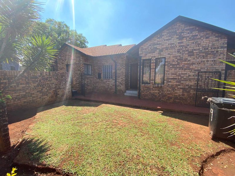Rear view of a face brick house featuring a tiled roof, security bars on windows, and a private garden area with a paved walkway.