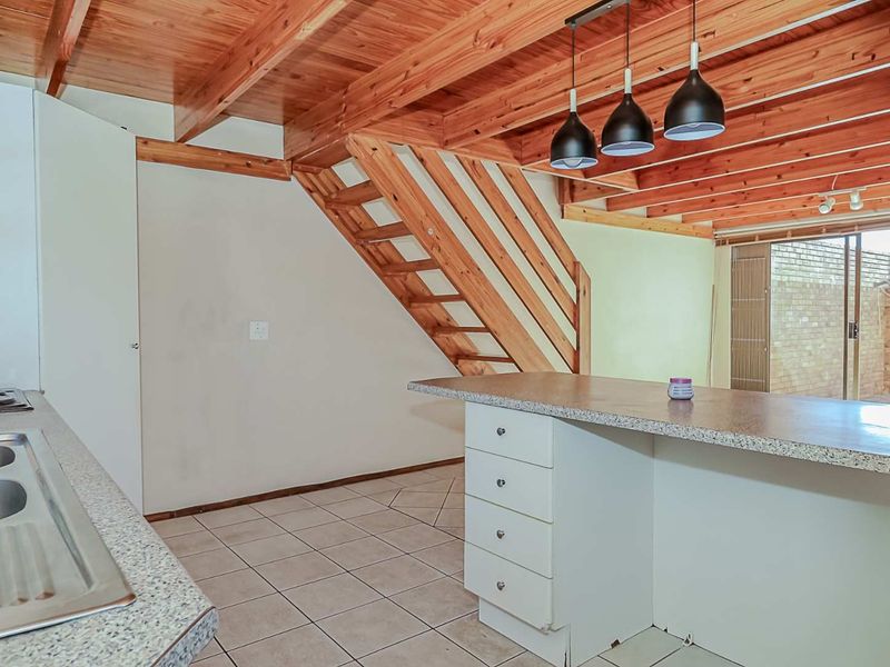 Open plan kitchen and living area featuring exposed timber ceiling beams, a timber staircase, and a functional kitchen island with built-in hob.