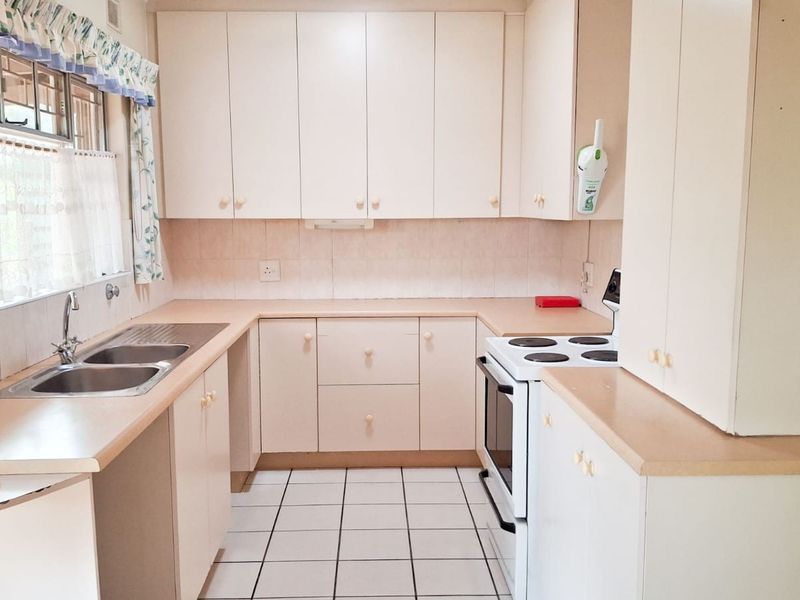 A functional kitchen featuring laminate countertops, ample built-in cabinetry, a double bowl stainless steel sink, and a freestanding electric stove with tiled flooring.