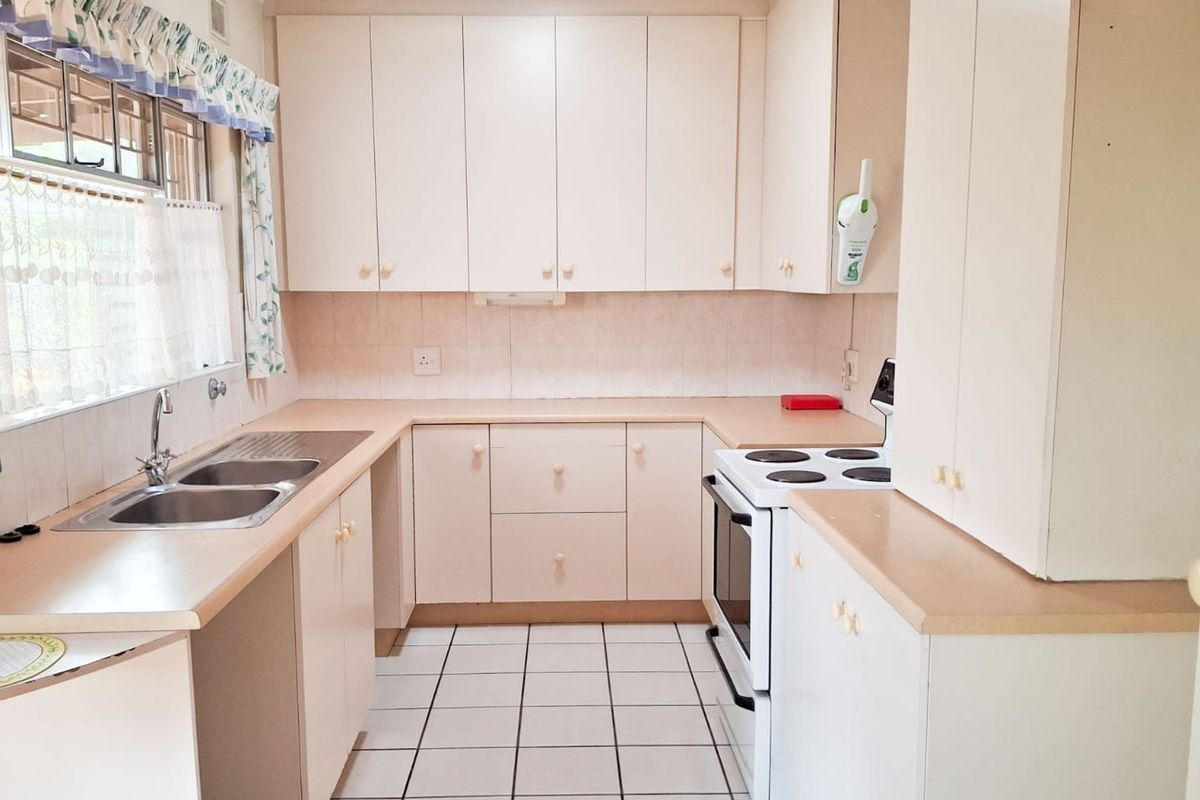 A functional kitchen featuring laminate countertops, ample built-in cabinetry, a double bowl stainless steel sink, and a freestanding electric stove with tiled flooring.