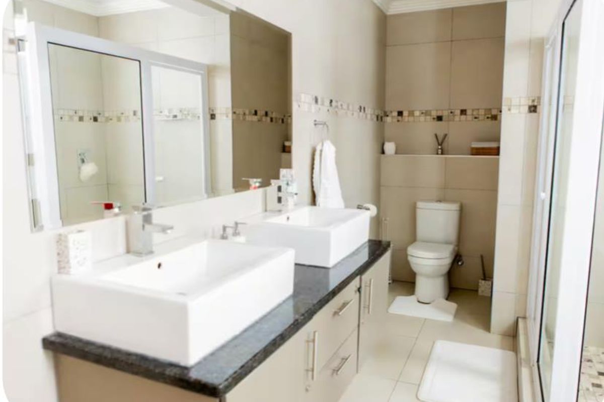 Modern bathroom featuring a double vanity with vessel sinks, large wall-mounted mirror, tiled walls with decorative mosaic accents, and a separate toilet area.