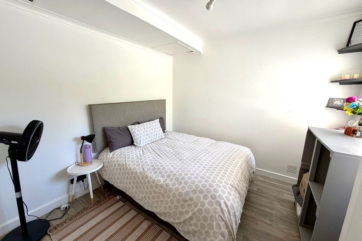 A functional bedroom featuring light-toned laminate flooring, neutral walls, and built-in shelving, providing a clean and versatile space.