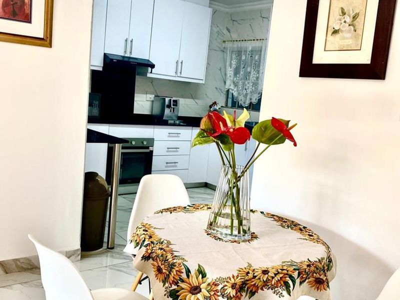 An open-plan dining area leading into a modern kitchen featuring white cabinetry, built-in appliances, and marble-look floor tiles.