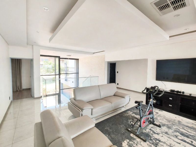 Spacious living area featuring a modern recessed ceiling, tiled flooring, and a glass balustrade overlooking the lower level.