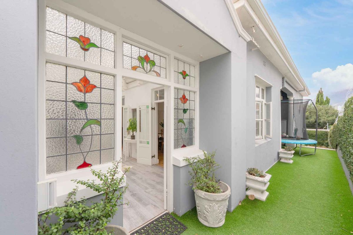 A well-maintained rear exterior view featuring a paved area with artificial lawn, classic stained glass windows, and access to the interior living space.