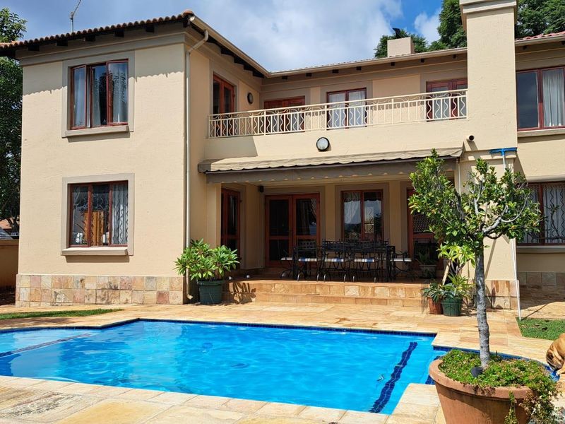 Rear view of a two-story house featuring a swimming pool, stone-paved patio, and an upper-level balcony with metal railings.