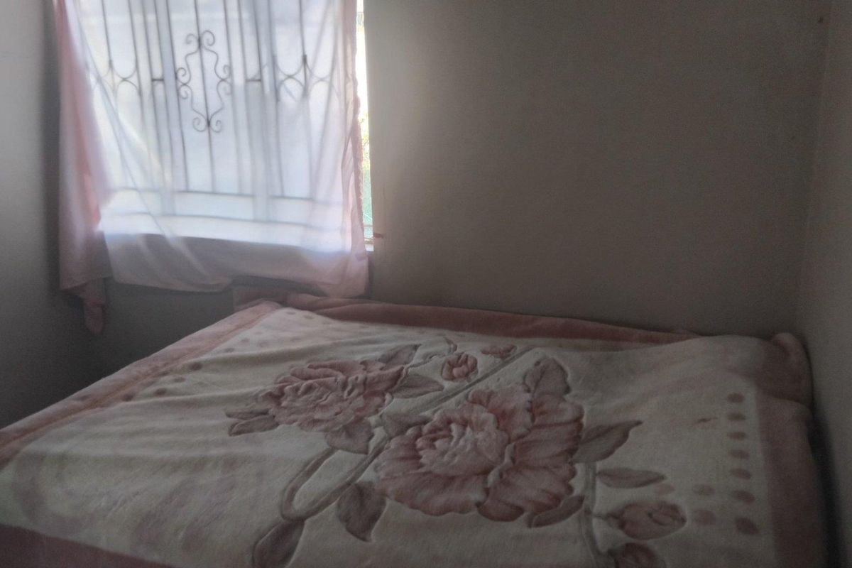 A compact bedroom featuring a window with security bars and natural light.